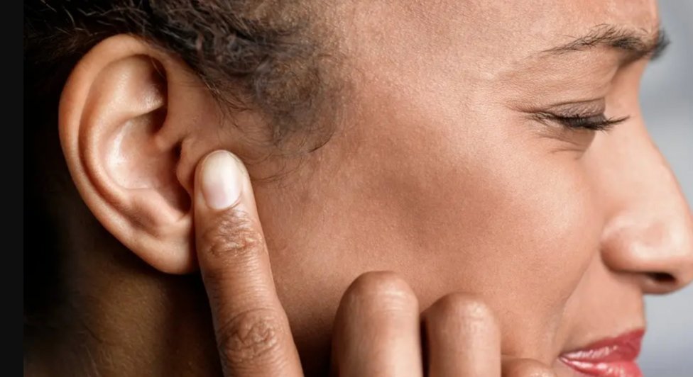 A woman shuts her eyes and puts her finger on her ear.