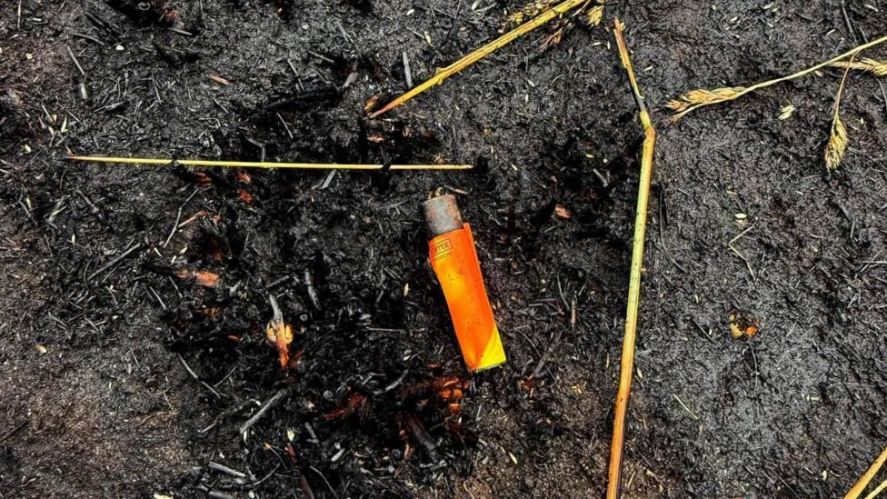 An orange lighter left on blackened, burnt ground