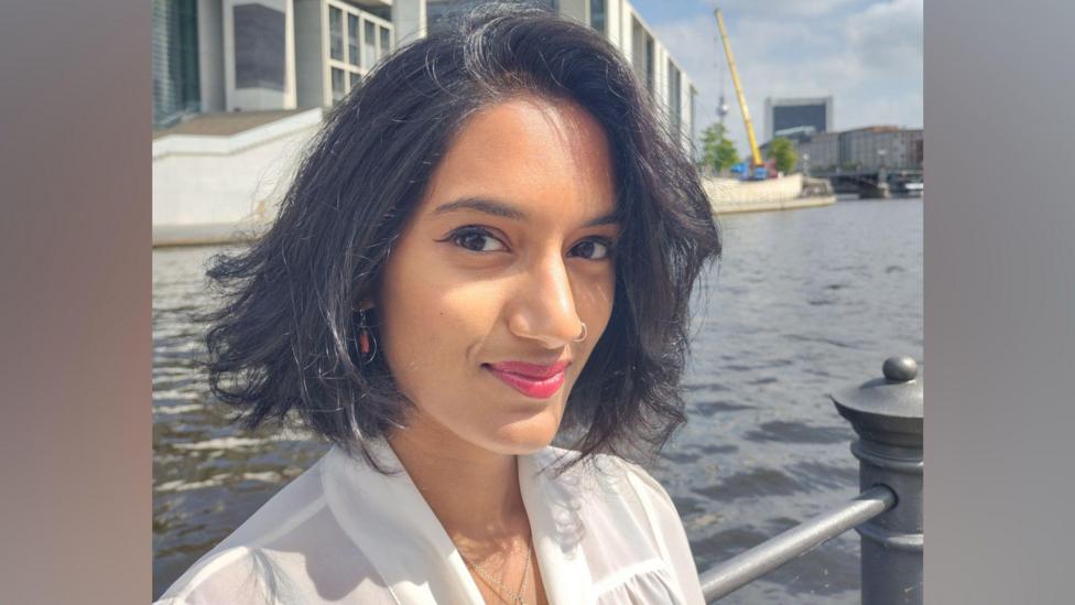 A 'selfie' of a woman wearing a white blouse. She has short brown hair and she is smiling.