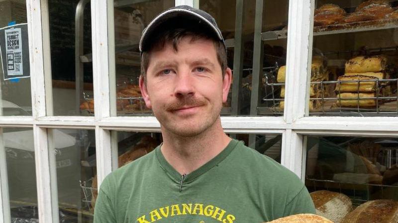 A man, who has short brown hair and a moustache, wearing a cap and a green t-shirt.