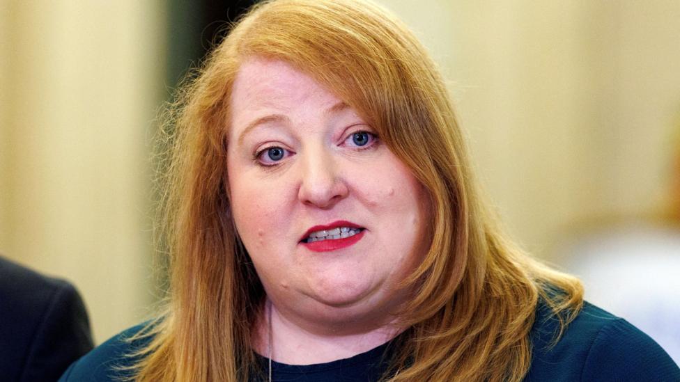 Naomi Long with red hair and a blue top.