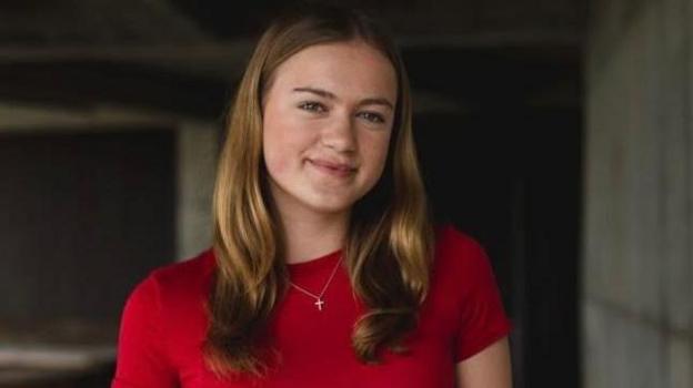 Miriam smiles at the camera. she is wearing a red top and had blonde hair