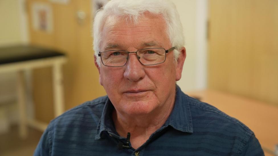 Ged Cashley is wearing a blue shirt and glasses. The 72 year old suffered a cardiac arrest in 2018 and now has annual health checks.