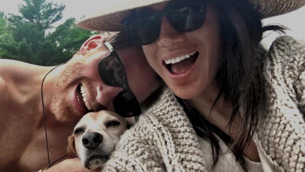a close-up photo of Harry and Meghan laughing with a dog in between them