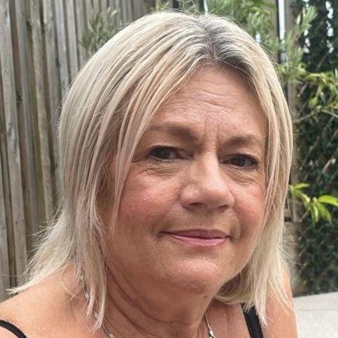 Jane Roberts has blonde shoulder length hair. She is photographed outside in a garden. She is smiling and looking at the camera.