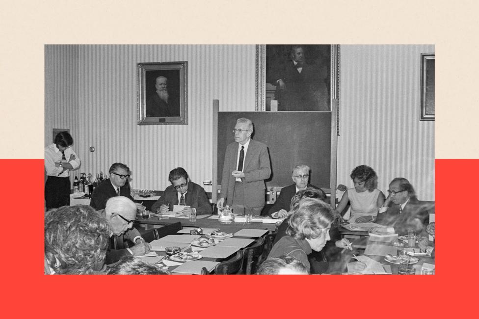 Hans Asperger standing up at a conference. He wears a light suit and is surrounded by other delegates. The photograph is black and white