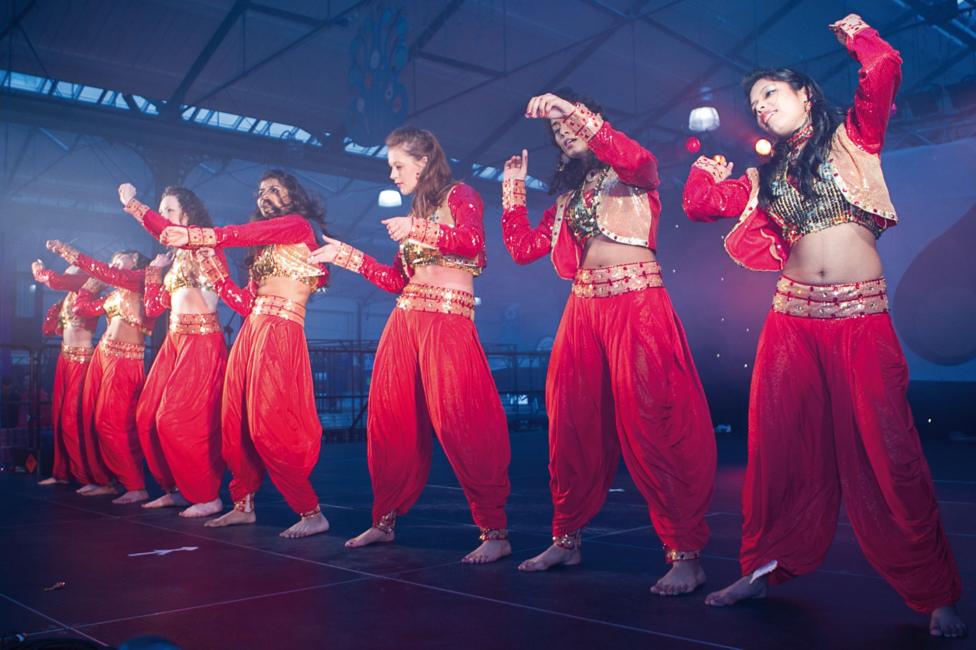 Seven women in red costumes standing on stage