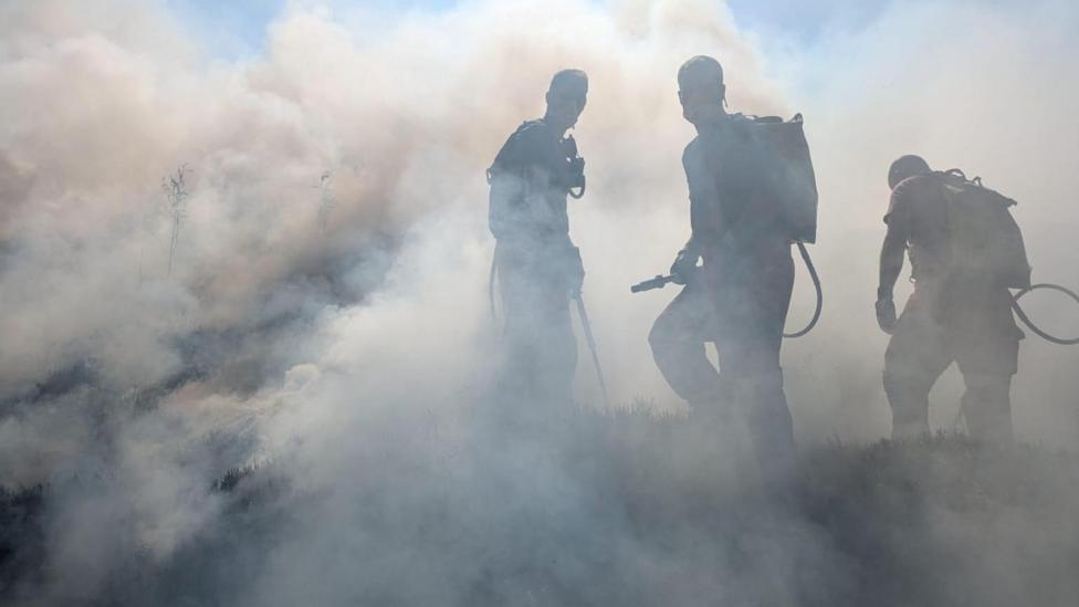 Three people with firefighting equipment in smoke during the firefighting effort earlier this month.