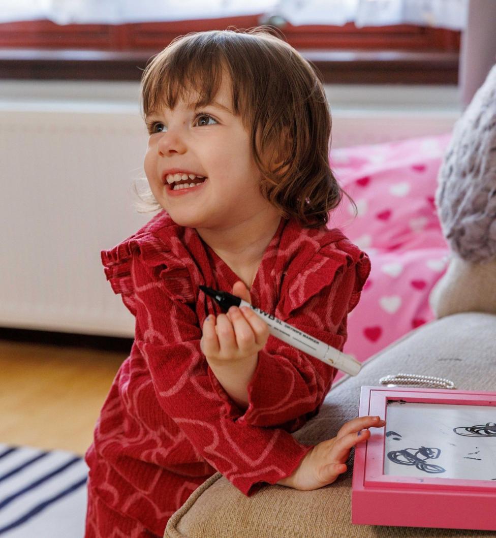 A young girl in a red outfit playing with an etch o sketch type toy in a living room