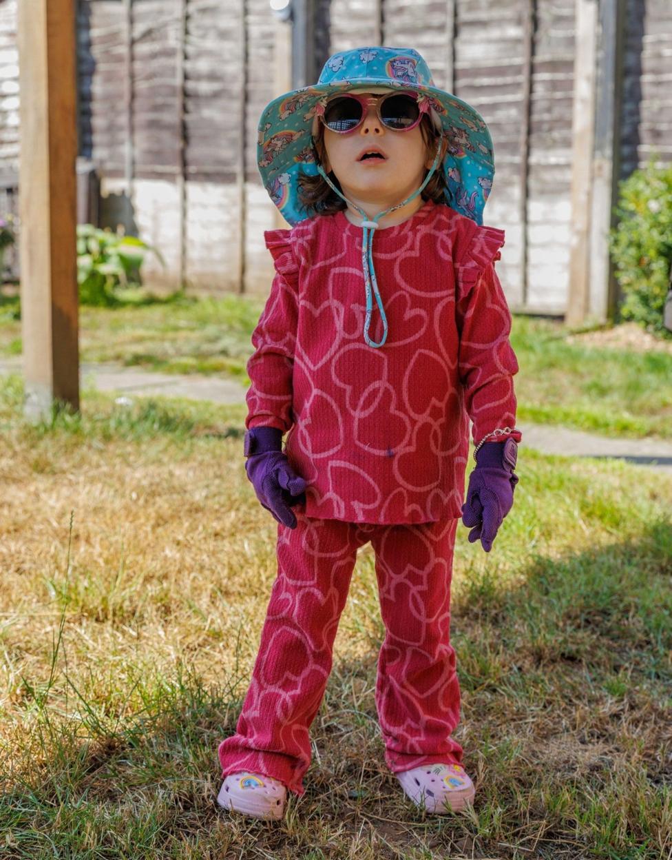 A child in a red outfit wearing a sun hat, gloves and sunglasses outdoors