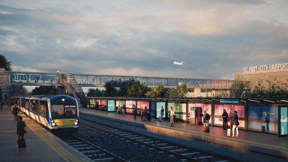 A train stop. On the left, there are people waiting at a platform, where a train is stationed. There are also people waiting on the opposite platform. In the background, there is building with a large sign which reads 'BELFAST CITY AIRPORT'. There is a white plane flying overhead. There is also a bridge-tunnel above the tracks which leads to the building with the 'BELFAST CITY AIPORT' sign.