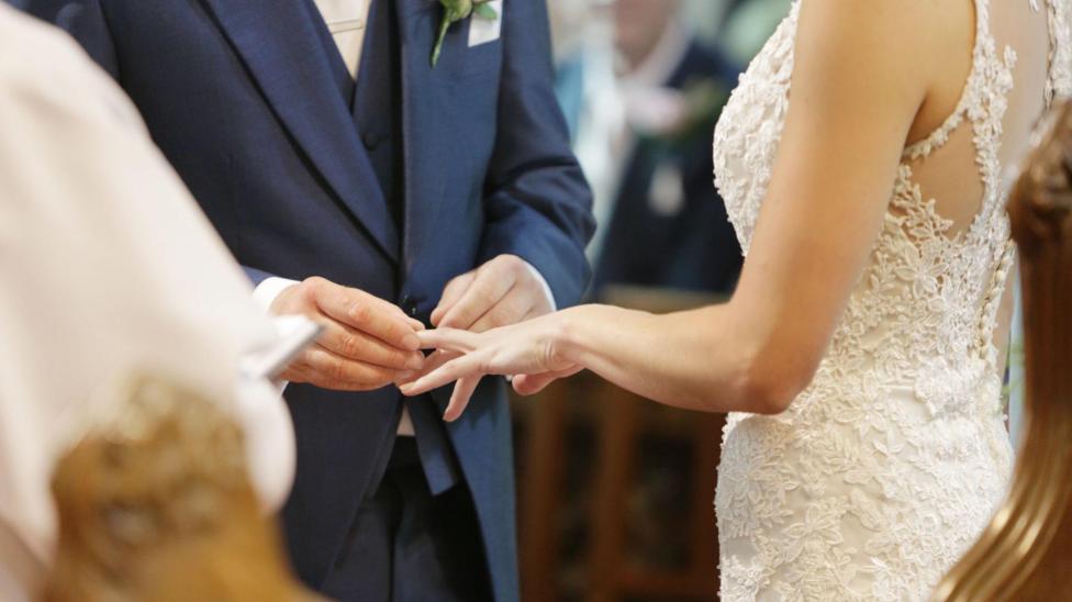 A groom is putting a wedding ring on a bride's finger