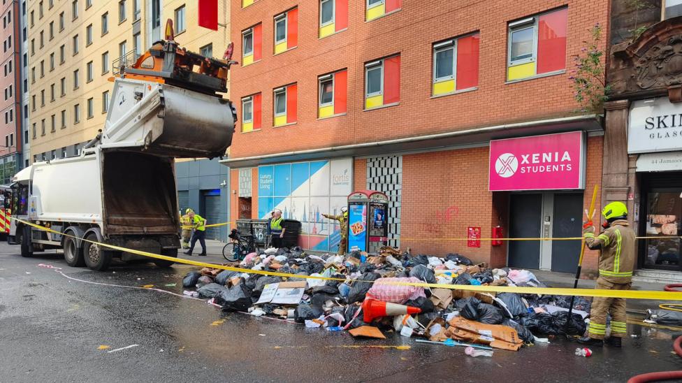 A bin lorry on Glasgow's Jamaica Street, with a big pile of rubbish tipped out on to the road. Firefighters are inspecting the rubbish.
