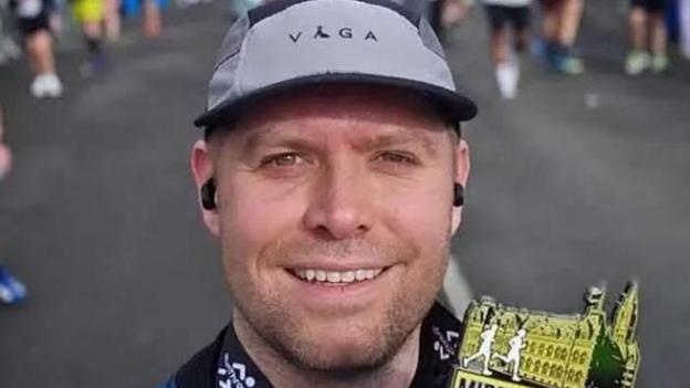 PC Blades takes a selfie with a medal for completing a run in Middlesbrough. He has neat stubble and is smiling, with a grey running cap on his head.