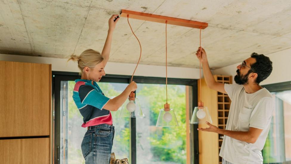 Young woman and man adjusting hanging lights in a kitchen