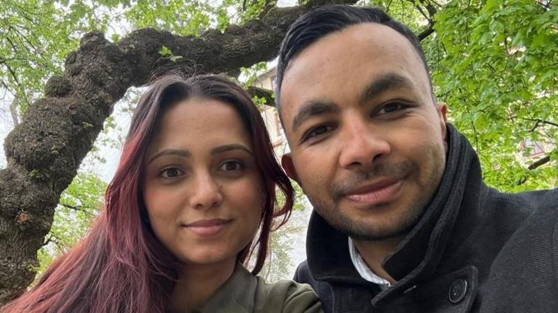 A selfie of a man and a woman sitting beneath a tree.