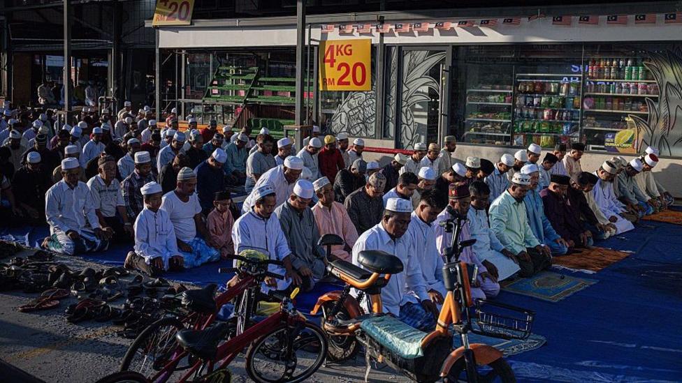 SELANGOR, MALAYSIA - JUNE 07: Rohingya Muslims gather and pray in front of a wholesale market during Eid al-Adha on June 07, 2025 in Selangor, Malaysia. Among those participating are Rohingya refugees who, despite facing legal and social challenges, continue to uphold their cultural and religious practices in Malaysia, including the observance of Islamic festivals as part of their faith. Eid al-Adha, also known as the "Festival of Sacrifice," commemorates Prophet Ibrahim's willingness to sacrifice his son in obedience to God, a devotion honored through the ritual slaughter of livestock, with the meat distributed among family, friends, and those in need. (Photo by Annice Lyn/)