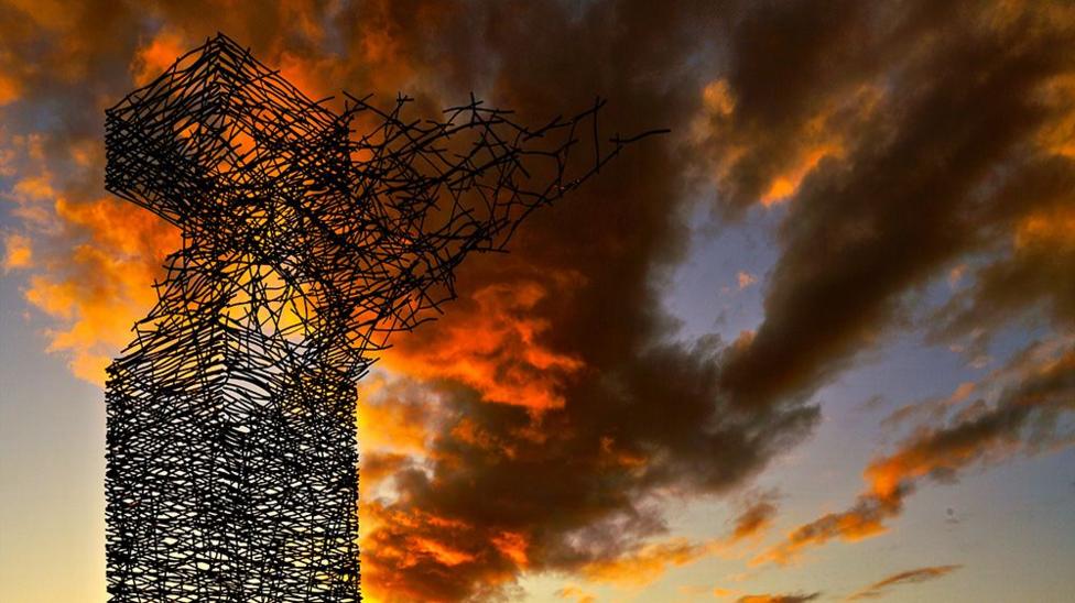 The Airdrie Sky Tower stands in silhouette against a dramatic sunset sky, with vivid orange and red clouds illuminated by the setting sun.
