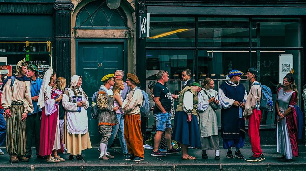 People in colourful period costumes stand and chat along South Bridge during the Edinburgh Fringe.