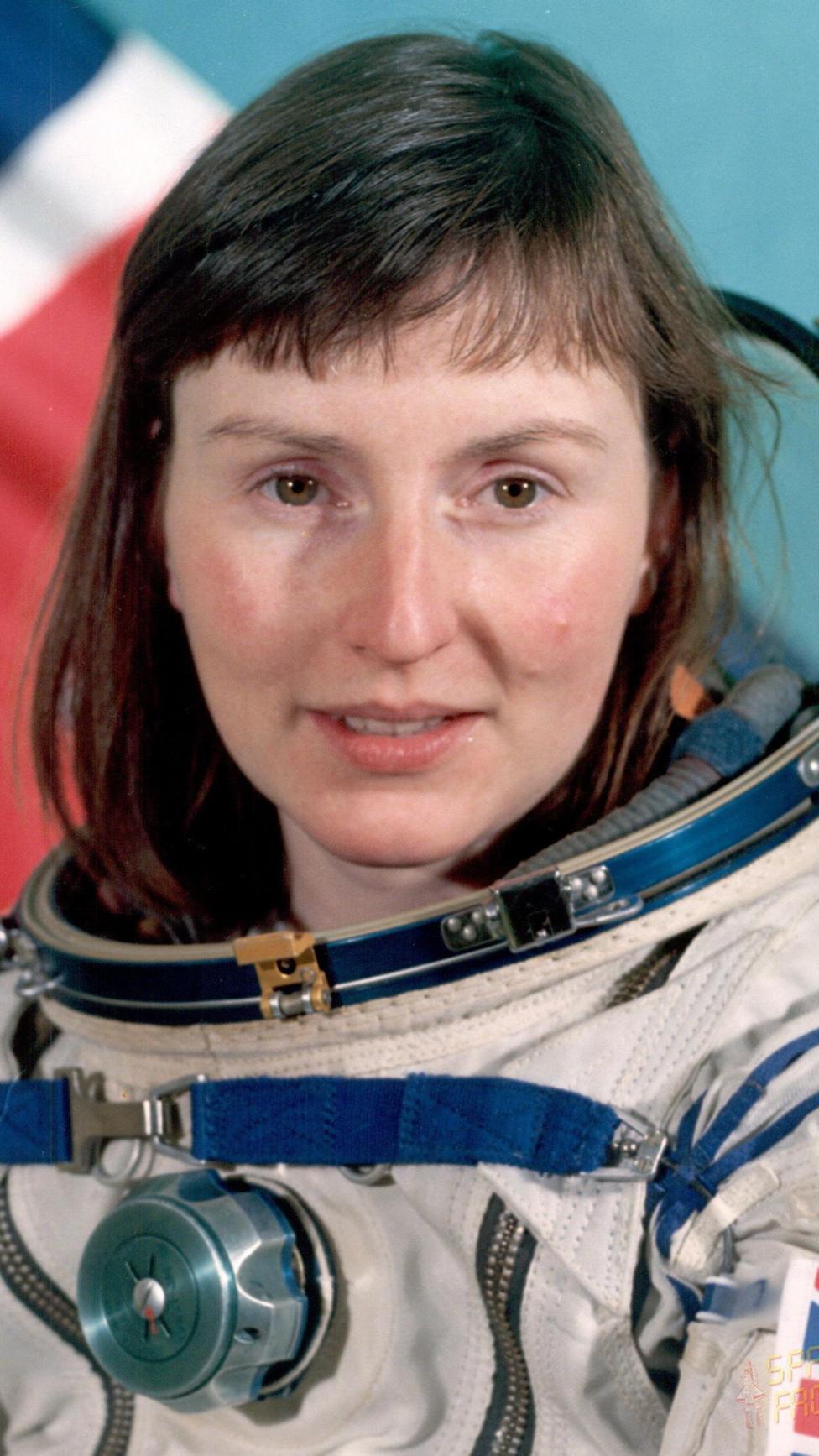 An official head and shoulders portrait-style photo of Helen Sharman wearing a space suit minus the helmet. She has shoulder length dark hair with a straight fringe. Part of the Union Flag, also known as the Union Jack, is just recognisable in the background.