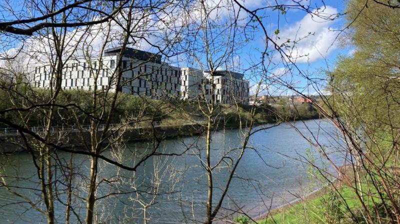 A river that has green trees surrounded by it and near a white building which is the True Student building in Swansea.