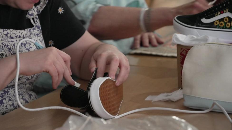 Someone holds a glue gun against a black Converse-like shoe.