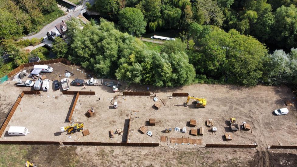 A drone image of diggers at the site, which is surrounded by brown fencing.