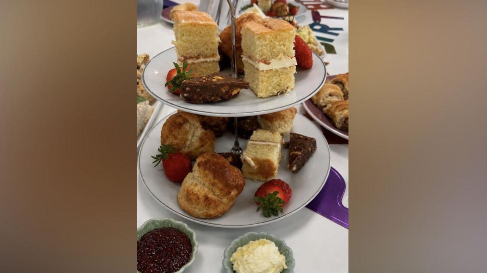 A tea set with cakes, scones and strawberries on the plates.
