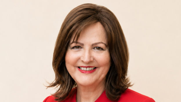 A woman called Jane Malyon. She has shoulder length brown hair in a bob style. She has a red top on and red lipstick. She is smiling with her teeth showing.
