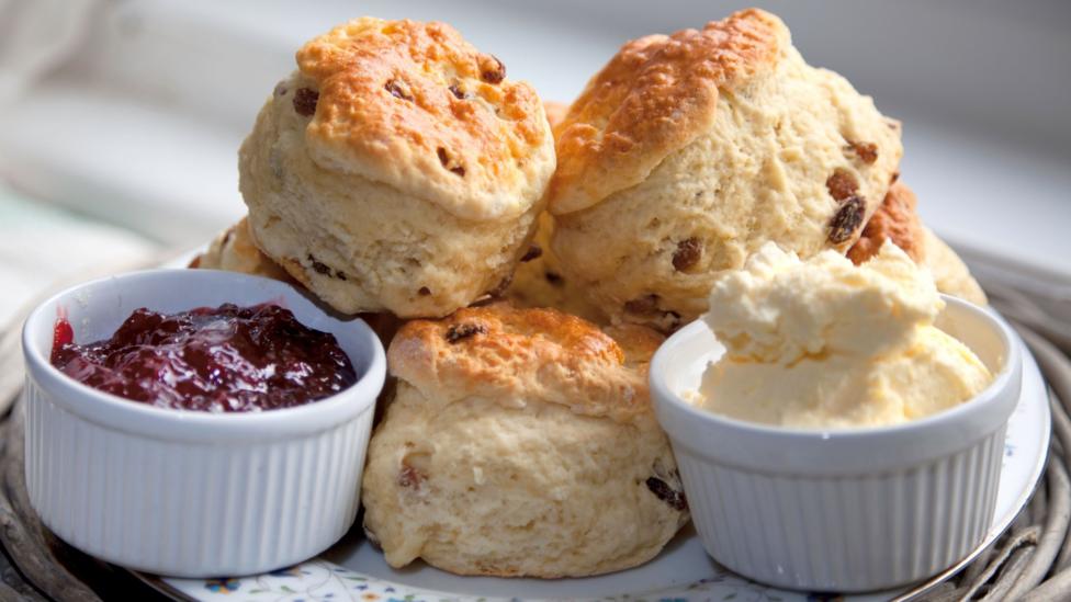A plate of scones with ramakins of jam and clotted cream.