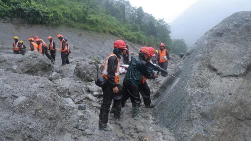 People in hardhats and high-vis drilling into boulders in a quarry.