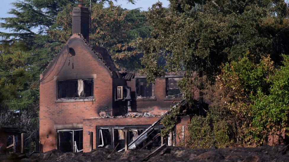 A burnt-out house with trees in the foreground and background