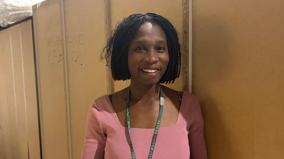 Esther Baffa-Isaacs smiling at the camera, in the background are the back of shelves.