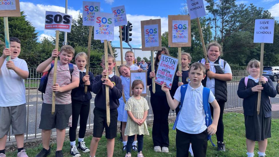 Around a dozen younger children hold protest signs in the air