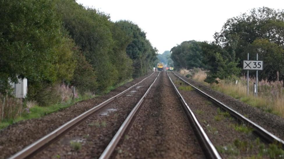 Image shows a view of a railway line, heading towards a vanishing point on thre horizon. A train can be seen in the distance.