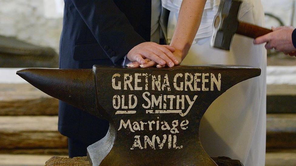 The Gretna Green marriage anvil being struck while a couple hold hands on top of it