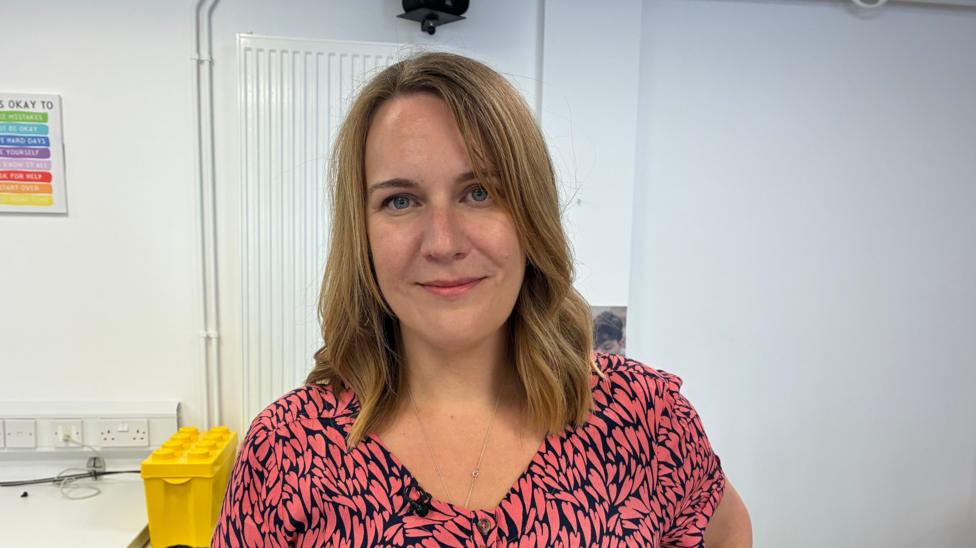 Councillor Gemma Furnivall stading in her second hand shop in front of a white wall with a box of toys in the background.