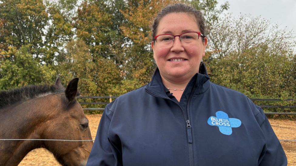 Vicki Alford stands in a navy blue 'Blue Cross' jacket with a brown pony behind her in a field