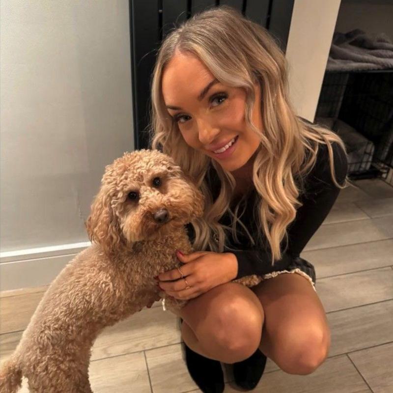 A woman with blonde hair poses with a light brown coloured dog. She is smiling into the camera as she crouches next to the pet.
