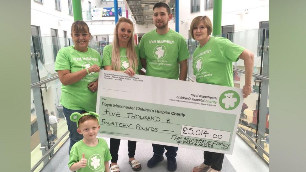 A group of people and a little boy are smiling while holding a giant cheque for £5,014. They are all wearing green T-shirts saying 'Team Humphrey' with an image of a teddy bear.