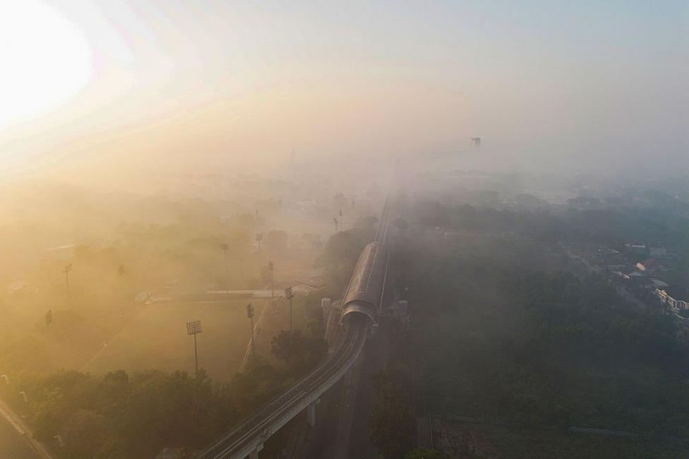 An aerial shot of a train line running through fields and shrouded in smoke