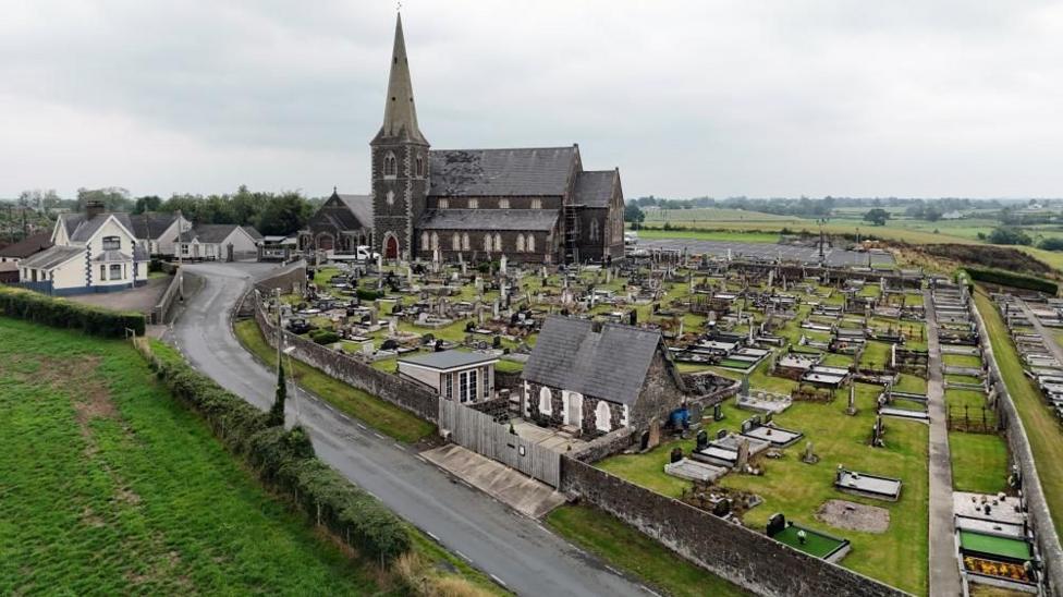 An aerial shot of a grey stone church and surrounding graveyard.