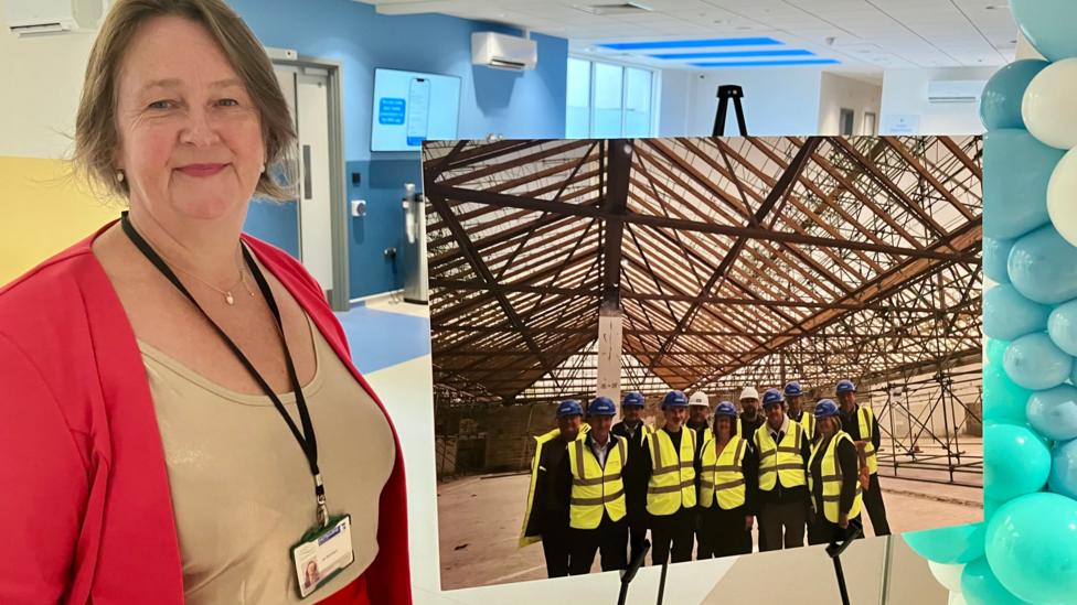 A woman in a red jacket stands alongside a large photograph of people in high vis jackets on a building site