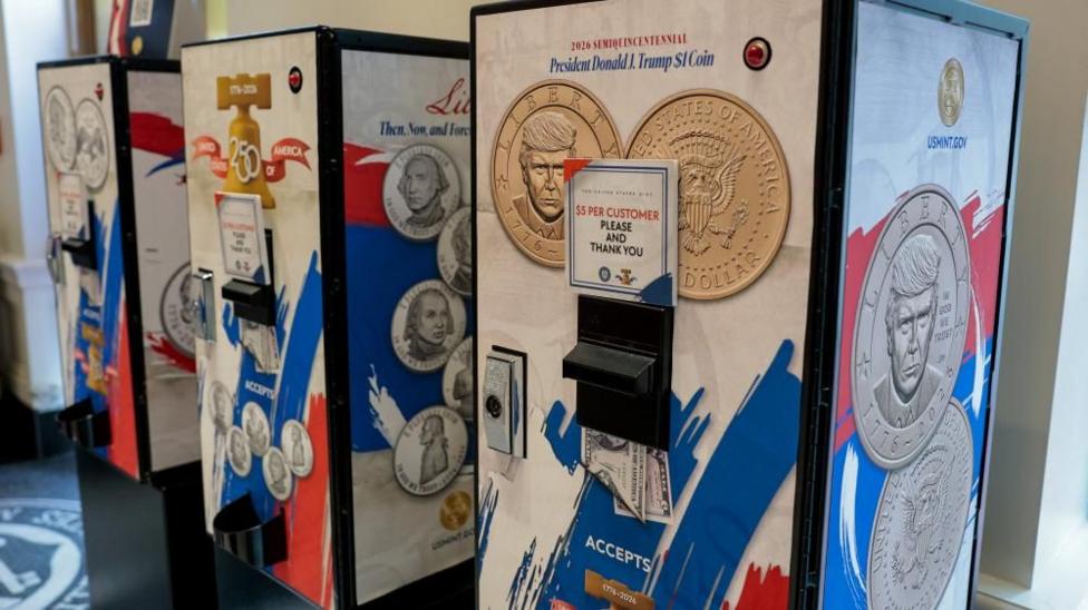 Three vending machines selling $1 coins featuring President Donald Trump's image at the US Mint Coin Store in Washington DC. On each machine there is a sign saying "$5 per customer please and thank you".