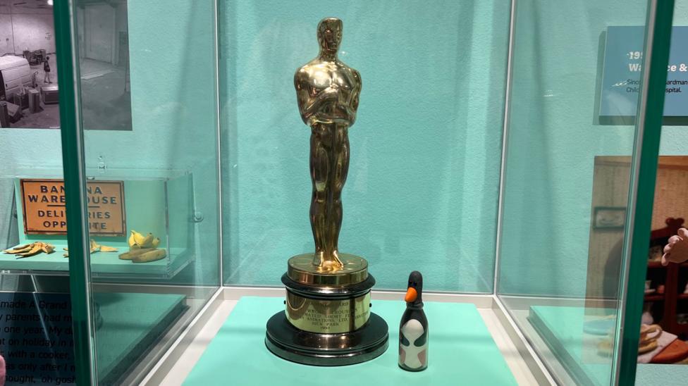 A picture of an Oscar in a cabinet with a model of a chicken beside it.