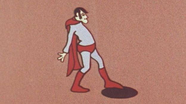 The original 'Aard Man' superhero 'dolt' that Peter Lord and Dave Sproxton created in 1972. He is wearing blue and red superhero clothes but has a sticking out belly and a strange facial expression. He looks like he is about to fall into a hole.