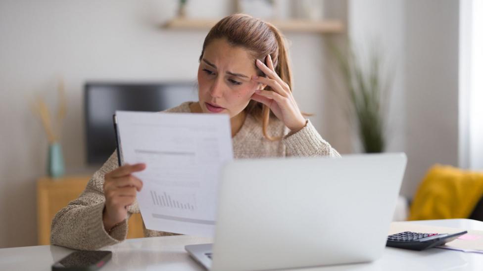 A woman looks at a letter revealing her bill with a stressed expression on her face.