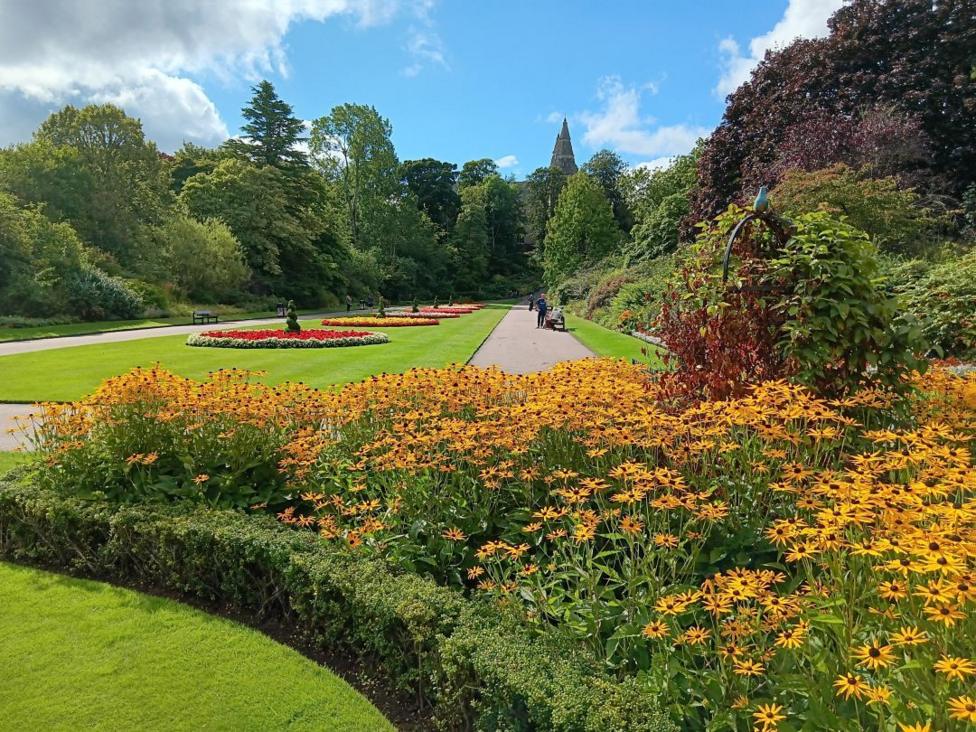 Seaton Park in Aberdeen. Bright coloured flowers fill the flower beds in the park. Trees line the paths and St Machar's Cathedral can be seen over the trees in the background.