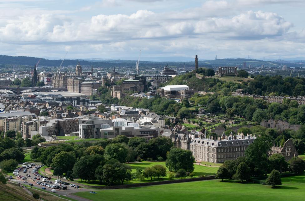 A view of Edinburgh's skyline with different buildings, parks and wooded areas.