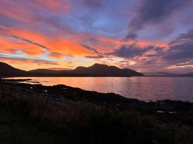 A sunrise over hills. The orange colours are reflected in the water.